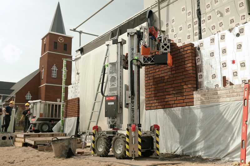 Un robot maçon Monumental en action sur un chantier de construction, pose de briques en cours devant une église européenne. Crédit photo : Monumental.